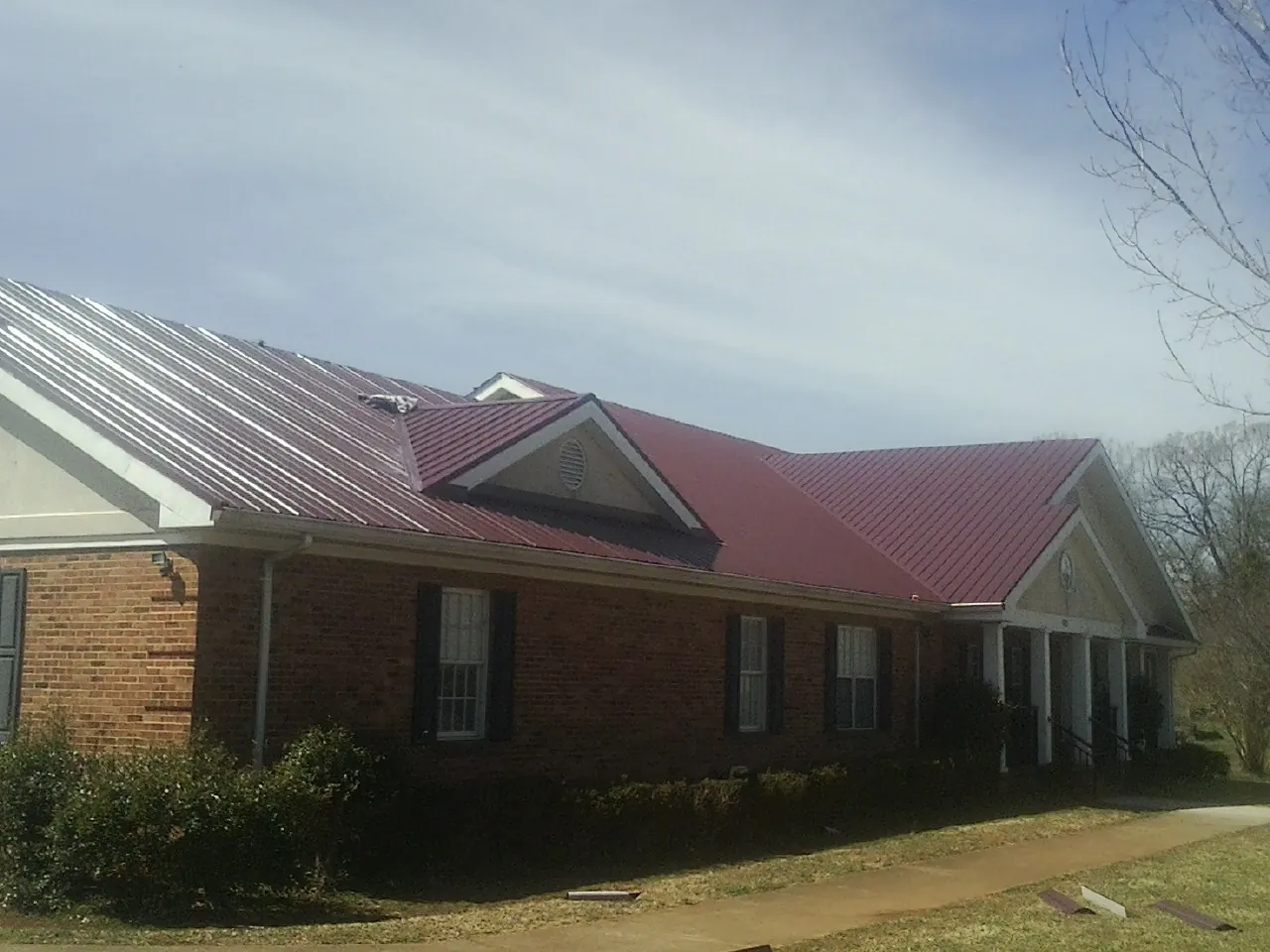 Red metal roof with gabled entries on a long brick building, from a Hail Damage Roof Repair job in Spring Grove