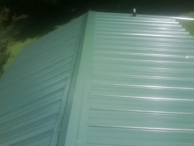 New green metal panels meeting at the ridge of a roof — Flat Roof Repair work by our crew in Spring Grove